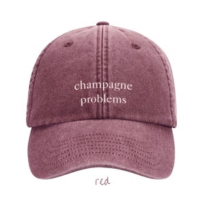 Könnte beinhalten: Eine rote Baseballkappe mit dem Text "Champagne-Probleme" in weiß gestickt.