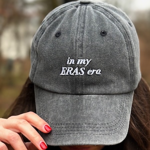 May include: A gray baseball cap with the text "in my ERAS era" embroidered in white on the front.