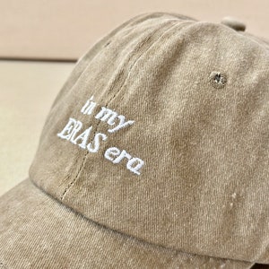May include: A brown baseball cap with white embroidered text that reads "in my ERAS era".