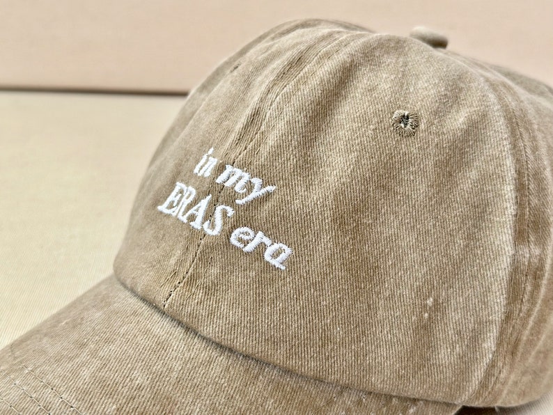 May include: A brown baseball cap with white embroidered text that reads "in my ERAS era".