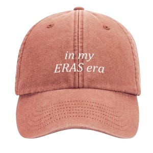 May include: A dusty rose colored baseball cap with white embroidered text that reads "in my ERAS era".