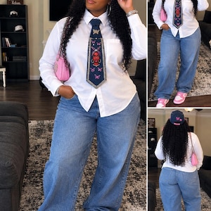 May include: A white long-sleeved button-down shirt, blue denim jeans, and pink sneakers. The outfit includes a dark denim baseball cap and a matching dark denim necktie, both featuring a graphic of a face with a headwrap and pink butterflies.