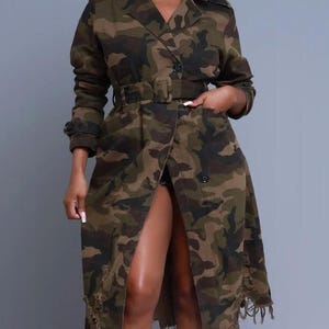 May include: A camouflage-patterned trench coat with a double-breasted design, a belt, and a frayed hem. The coat features a classic collar, button closures, and pockets. The color palette includes shades of green, brown, and black.