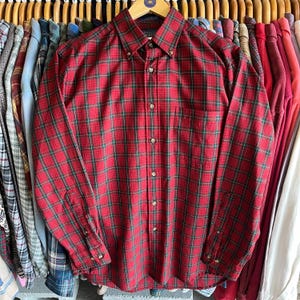 May include: A red and green plaid long-sleeve button-down shirt. The shirt has a pocket on the left side.