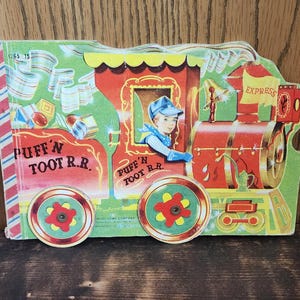 May include: Vintage children's toy train with a red engine and green accents. The train features a young boy in the driver's seat and the words "Puff 'N Toot R.R." and "Express". The toy is made of cardboard.