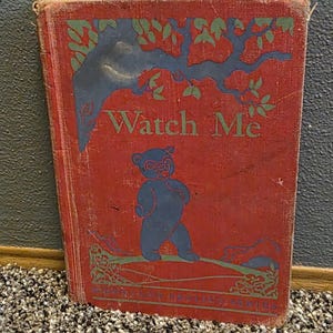 May include: Vintage children's book titled "Watch Me" with a red cover. The cover features a blue bear illustration under a tree design with green accents. The book is worn, suggesting age and use.