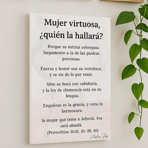 Puede incluir: Un lienzo blanco con texto en español, "Mujer virtuosa, ¿quién la hallará?" (Mujer virtuosa, ¿quién la hallará?). La impresión está rodeada de arte enmarcado y una planta verde. El texto es de Proverbios 31:10, 25-26, 30.