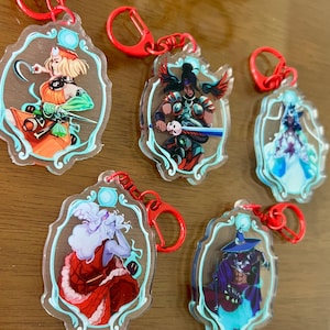 Peut inclure: Plusieurs porte-clés en acrylique avec des illustrations de personnages fantastiques. Chaque porte-clés a un design unique avec des couleurs vives, un fermoir rouge et une bordure décorative. Les personnages sont représentés dans diverses poses et tenues.