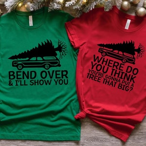 May include: Two short-sleeved Christmas-themed t-shirts. One is green with the text "BEND OVER & I'LL SHOW YOU" and a graphic of a car carrying a Christmas tree. The other is red with the text "WHERE DO YOU THINK YOU'RE GONNA PUT A TREE THAT BIG?"