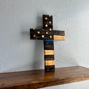 May include: Wooden cross with an American flag design and a thin blue line representing law enforcement. The cross is made of reclaimed wood and has a rustic finish.