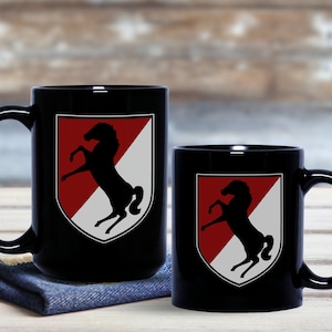 May include: Two black ceramic mugs with a white and red shield design featuring a black silhouette of a rearing horse. The shield has a white stripe across the red background.