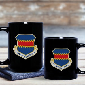 May include: Two black ceramic mugs with a blue, red, and yellow crest and the text "VIDEMUS OMNIA".