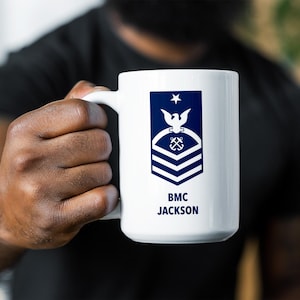 May include: White ceramic mug with a blue and white Coast Guard Chief Petty Officer insignia and the text "BMC JACKSON".