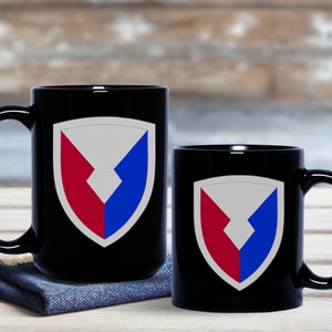 May include: Two black ceramic mugs with a white, red, and blue shield design. The shield has a white background with a red and blue chevron pattern.