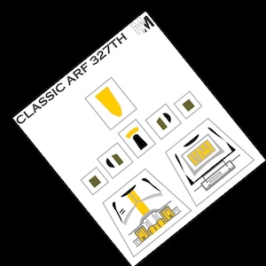 May include: A white sheet with the text "CLASSIC ARF 327TH" and various geometric shapes in yellow, black, and olive green. The shapes include rectangles, squares, and curved lines, all set against a black background.