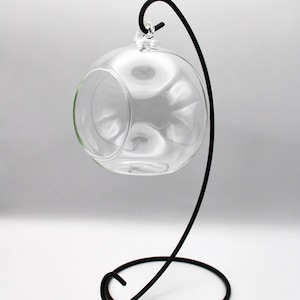 May include: A clear glass globe with a metal stand. The globe is suspended from the stand by a metal loop. The stand is black and has a circular base.