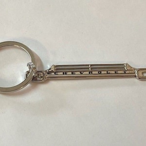 May include: A silver key chain with two keys and a Chevrolet logo charm. The charm is a silver replica of a classic Chevrolet grille.