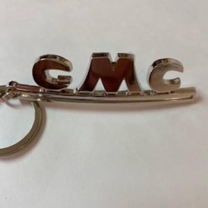 以下が含まれることがあります： 太字の文字でGMCと書かれた銀色の金属製のキーホルダーです。