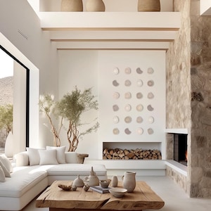 Può includere: Un divano bianco a sezione con un tavolino da caffè in legno in un soggiorno moderno. La stanza presenta un camino in pietra, una grande finestra e una parete con una mostra di cerchi in ceramica beige e marrone.