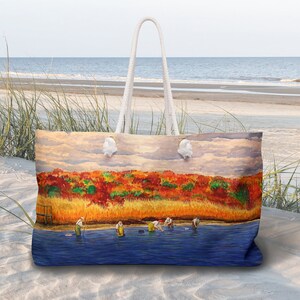 May include: A white tote bag featuring a colourful painting of a beach scene. The painting shows a group of people wading in a body of water with a forest of red, orange and yellow trees in the background.