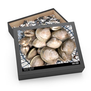 May include: A 500 piece jigsaw puzzle featuring a close-up of a basket full of clams. The puzzle box is black with white text that reads "16x20 Puzzle 500 pcs Ages 9+"
