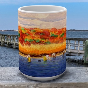 Peut inclure: Une tasse en céramique blanche avec une peinture colorée d'une scène d'automne avec des personnes dans l'eau. La scène comprend une jetée en bois et une étendue d'eau.