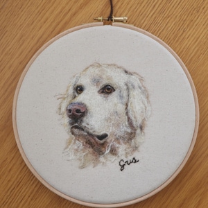 May include: A white needle felted portrait of a dog in a wooden embroidery hoop. The dog's name, "Gus", is embroidered below the portrait.