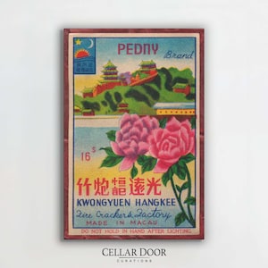 Könnte beinhalten: Gerahmter Vintage-Druck mit einer farbenfrohen Illustration. Das Kunstwerk zeigt eine Landschaft mit Gebäuden, Bergen und zwei großen rosa Pfingstrosen. Der Text enthält "PEDNY Brand" und "Fire Crackers Factory, Made in Macau."