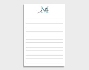 May include: A white notepad with horizontal grey lines. The top of the notepad features the name "Miller" in a script font, with the letter "M" in a light blue colour.