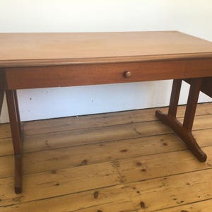 May include: A wooden drop leaf table with a single drawer and a light wood finish. The table has a simple design with rounded edges and a rectangular top.