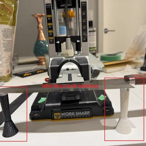 Może przedstawiać: System ostrzenia noży z dużym ostrzem i dwoma stabilizatorami. Stabilizatory są czarne i białe, a widoczny jest tekst "Work Sharp Knife Stabilizers". System znajduje się na białej powierzchni.
