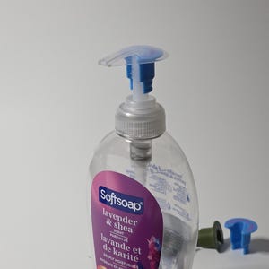May include: A clear plastic bottle of Softsoap hand soap with a lavender and shea scent. The bottle has a pump dispenser with a blue and white top.