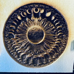 Puede incluir: Un diseño de sol y luna de madera con una talla detallada de un sol con rayos y un círculo de lunas alrededor.