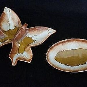 May include: A set of two ceramic butterfly-shaped dishes. The larger dish is shaped like a butterfly with brown and yellow glaze. The smaller dish is oval-shaped with a brown and white glaze.