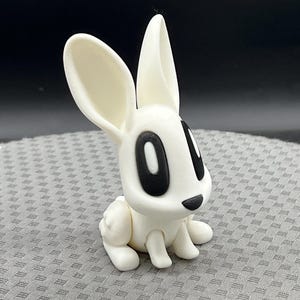May include: White rabbit figurine with large black eyes and a black nose. The rabbit is sitting on its hind legs with its front paws resting on its lap.