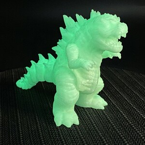 Op de afbeelding: Een groene, in het donker lichtgevende plastic dinosaurus met een stekelige rug en een wijd open mond.