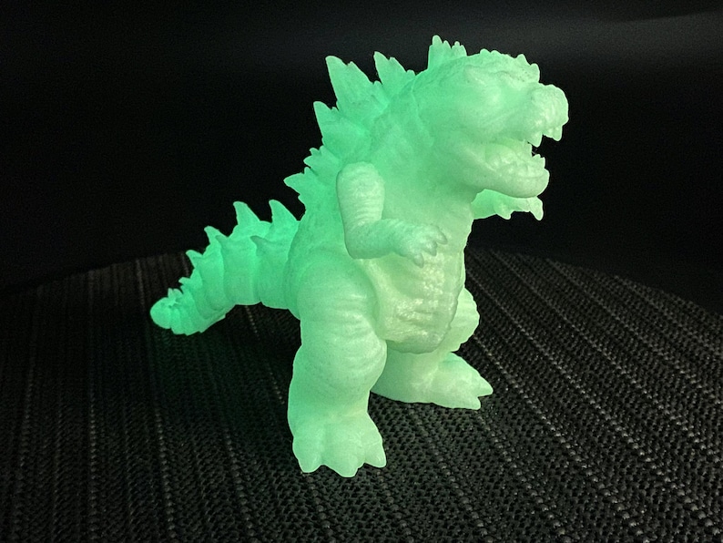 Op de afbeelding: Een groene, in het donker lichtgevende plastic dinosaurus met een stekelige rug en een wijd open mond.