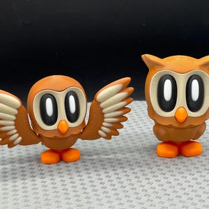 May include: Two brown owl figurines with white eyes. One owl has outstretched wings and the other is standing upright.