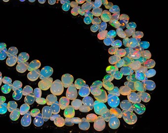 May include: Strands of opalescent opal beads. The beads are pear-shaped and strung together, displaying a range of colors including white, blue, green, and hints of pink and orange. The beads have a glossy finish and are set against a black background.