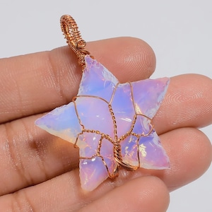 May include: A star-shaped pendant made from a translucent, opalescent stone, secured with copper wire. The stone has a soft, iridescent sheen with white, pink, and blue tones. The wire is intricately wrapped around the star, creating a loop for a chain.