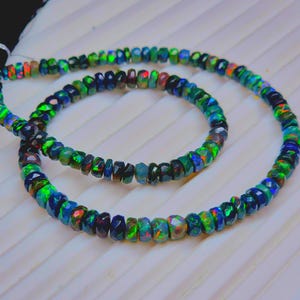 May include: Two strands of faceted opal beads in a variety of colors, including green, blue, and red. The beads are strung together to form a necklace or bracelet. The opals have a shimmering, iridescent quality.