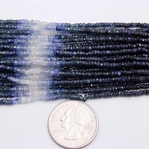 Può includere: Fili di perline di pietre preziose blu sfaccettate, che vanno dal blu chiaro allo scuro. Una moneta da un quarto di dollaro USA è inclusa come riferimento delle dimensioni. Le perline sono probabilmente per la creazione di gioielli.