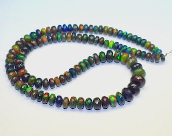 May include: A strand of faceted opal beads in a variety of colors, including green, blue, and orange. The beads are strung together, forming a necklace. The opal beads have a dark base color with flashes of iridescent color.