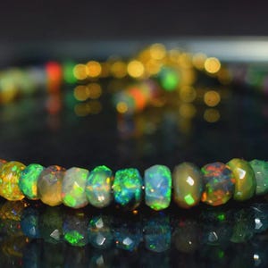 May include: A beaded bracelet featuring iridescent opal gemstones. The opals display a range of colors, including green, blue, red, and yellow. The bracelet is strung on a gold-colored chain and clasp.