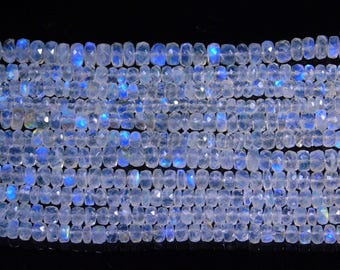 May include: Strands of faceted moonstone beads. The beads are a translucent white with flashes of blue and iridescent hues. The beads are rectangular in shape and strung together, creating a shimmering effect. The background is black.
