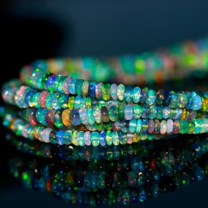 May include: Strands of colorful opal beads. The beads display a range of colors, including blue, green, pink, and yellow. The beads are small and round, and they are strung together to form a necklace or bracelet.