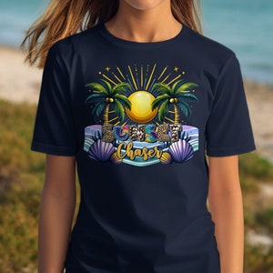以下が含まれることがあります： ネイビーブルーのTシャツ。カラフルなグラフィックデザインで、太陽、ヤシの木、そして「Sunset Chaser」の文字が特徴的です。貝殻とストライプのバナーがトロピカルなテーマを完成させています。ビーチ好きにぴったりのカジュアルTシャツです。
