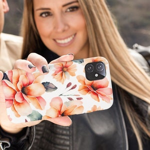 May include: A white phone case with a floral design featuring orange, pink, and green watercolour flowers. The case has a camera lens cutout with two black circles.