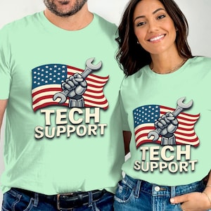 以下が含まれることがあります： アメリカ国旗、レンチを持ったロボットハンド、そして「TECH SUPPORT」の文字が描かれたグラフィックが特徴の、明るい緑色のTシャツ。2人の人が着ています。