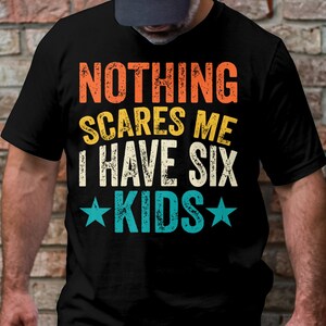 May include: Black t-shirt with a vintage-style graphic that reads "Nothing scares me I have six kids" with stars on either side of the word "kids".